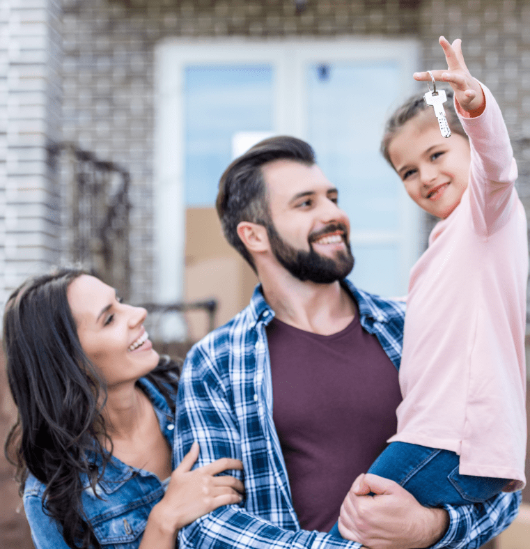 Homebuyers holding their child who is holding a house key in front of their new home