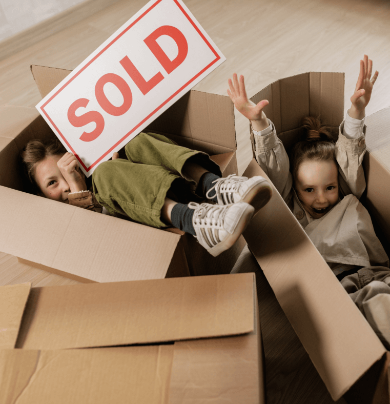Two children in empty boxes selling a "sold" sign in their new home in west chester